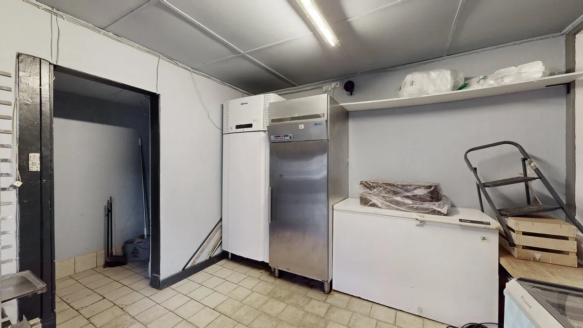 Køkken med køleskabe og lagerhylder, indretningsgenstande og en trappe med trækasser placeret i hjørnet