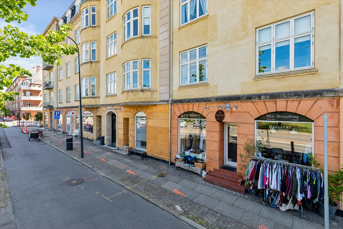 En række gule og hvide lejligheder med butikker og tøjvaskeriet Miss Moneypenny og Herreto på gadehjørnet på Strandvejen