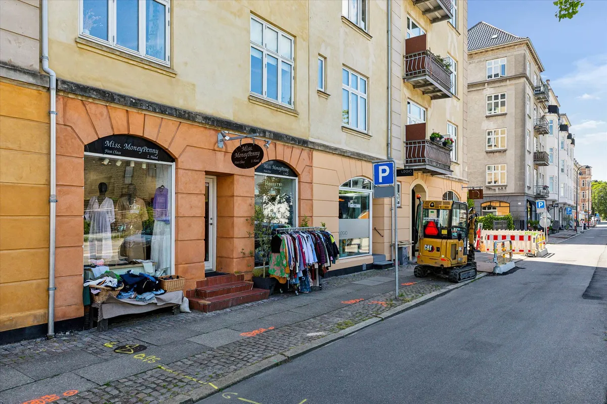 Københavnsgade med tøjbutik og parkeringsforbudsskilt, jordgravningsmaskine, rækkehuse og gågade med bollards og