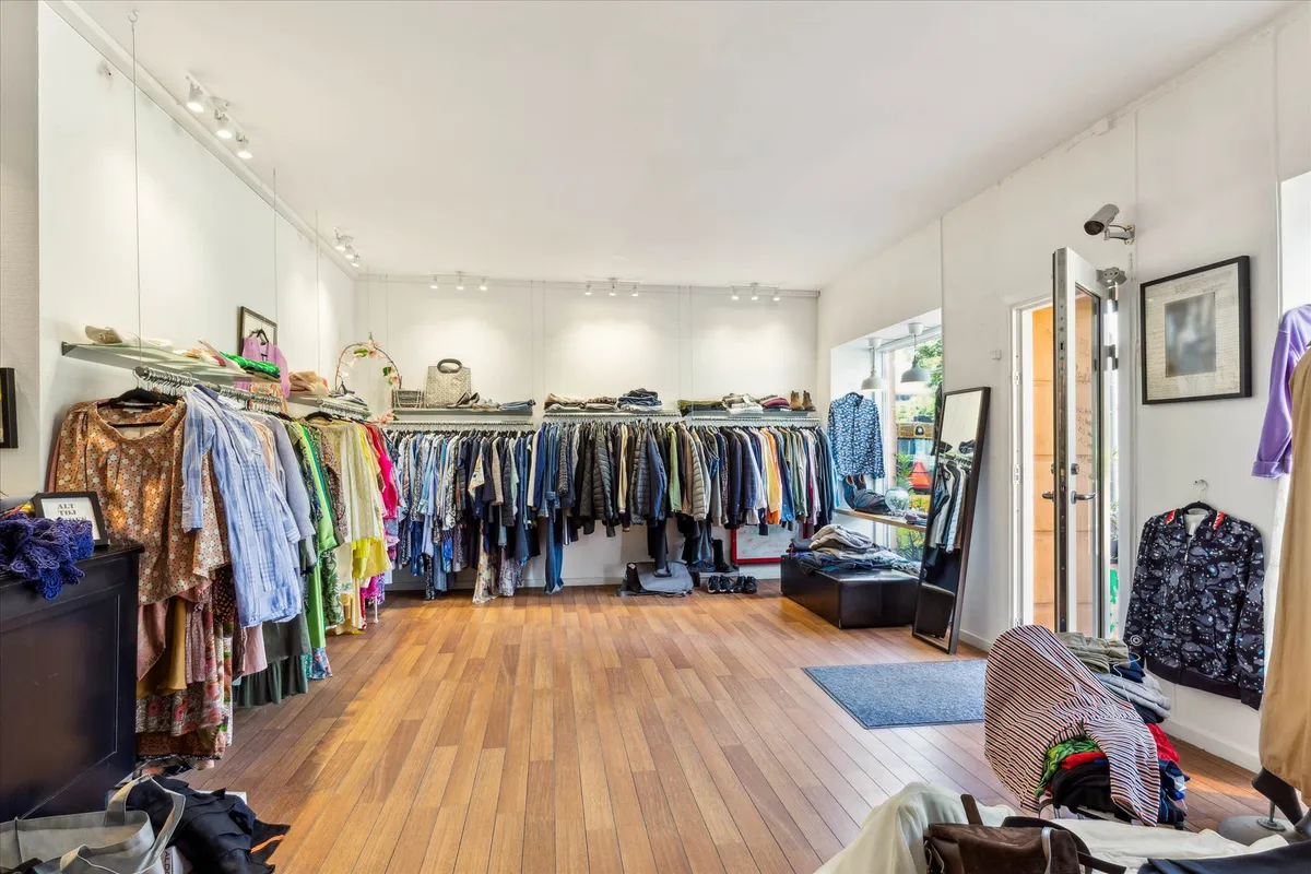 Butik med mange forskellige tøjsorter på hængere og i kurve, trægulv og flere indretningsgenstande