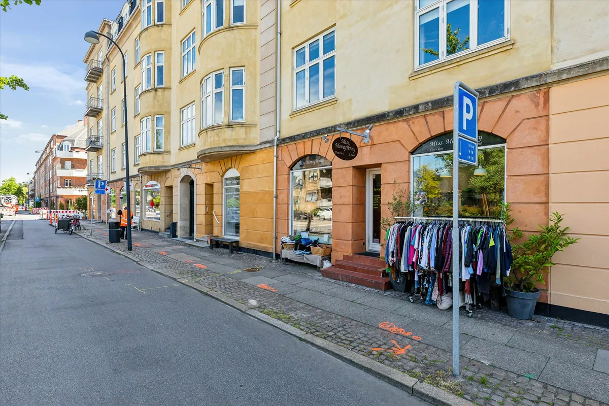 En tom gade med butikker, hvor den ene har tøj udstillet på gaden, parkeringsskilt og en søjle med skrift