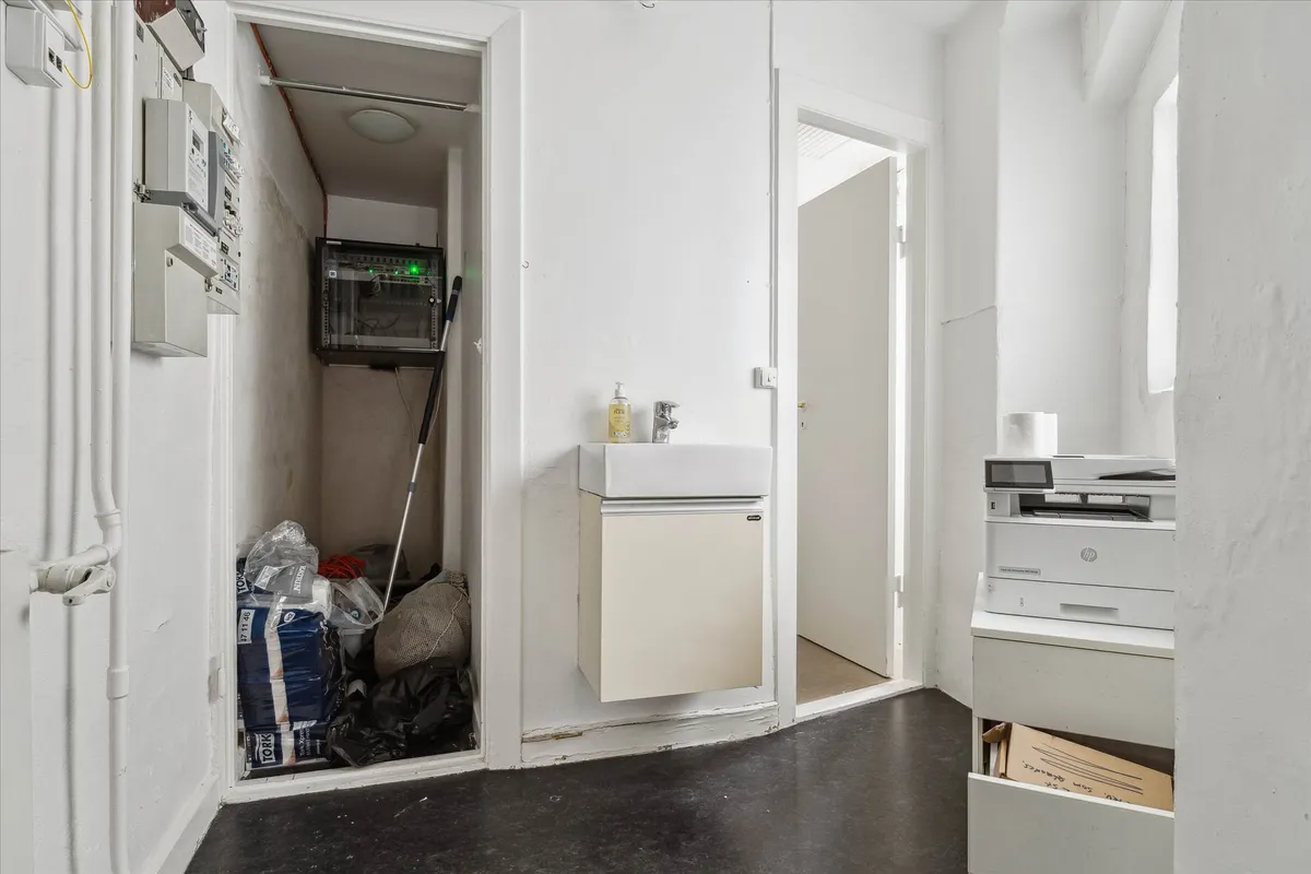 Hjørnerum med opvaskeblik, hvor der er en printer og papkasser i skabet, og der er et skab med udstyr på gulvet