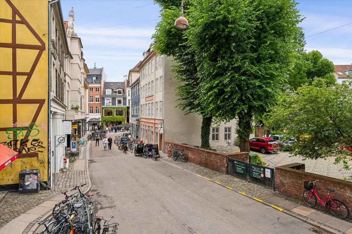 Bygninger med maleri, gaden med cykler, folk, og rødt og gult maleri på bygningen samt biler parkeret ved siden af