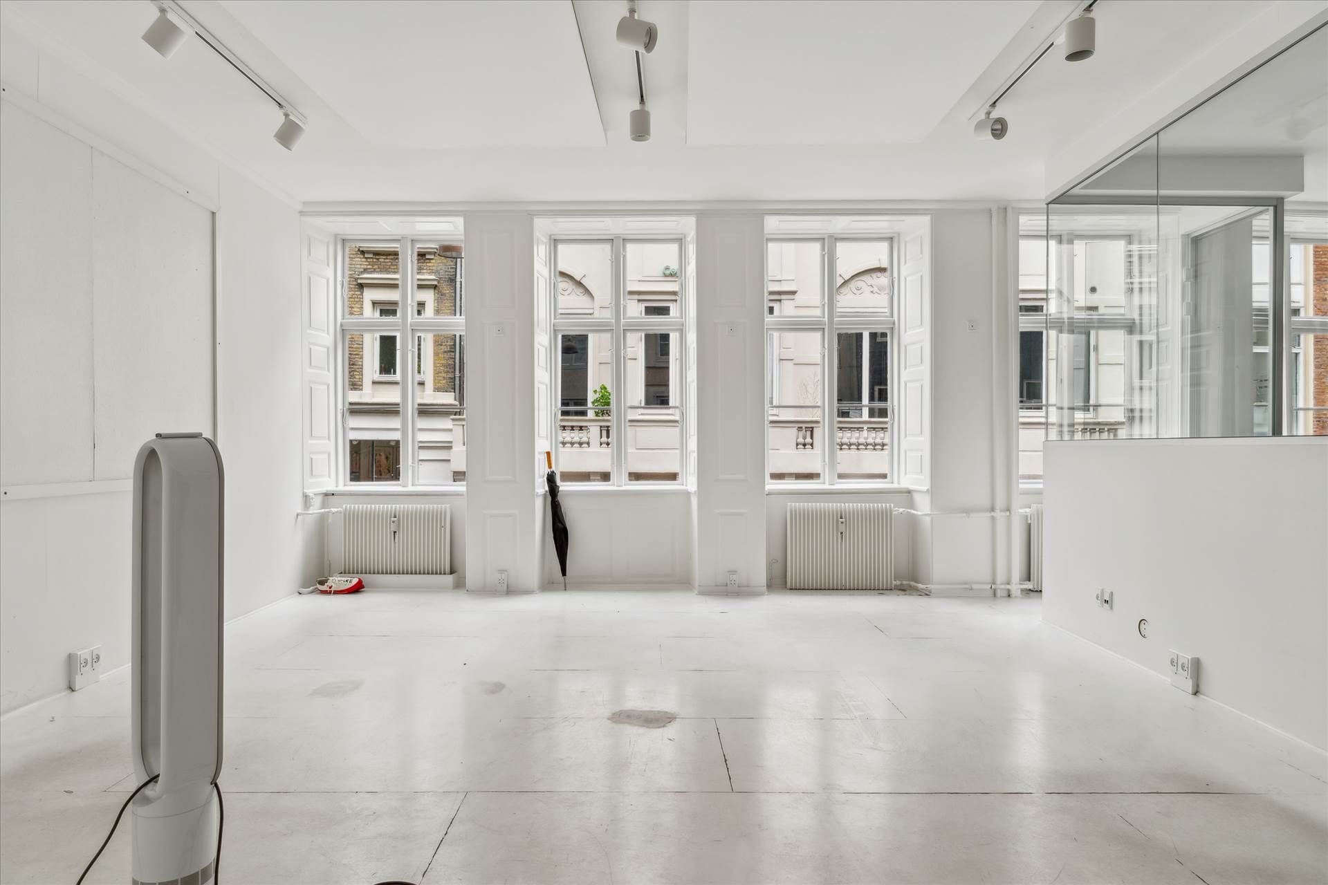 Et stort, lyserum med hvide vægge og gulv samt lysekroner og flere vinduer og radiatorer i hvide vægge