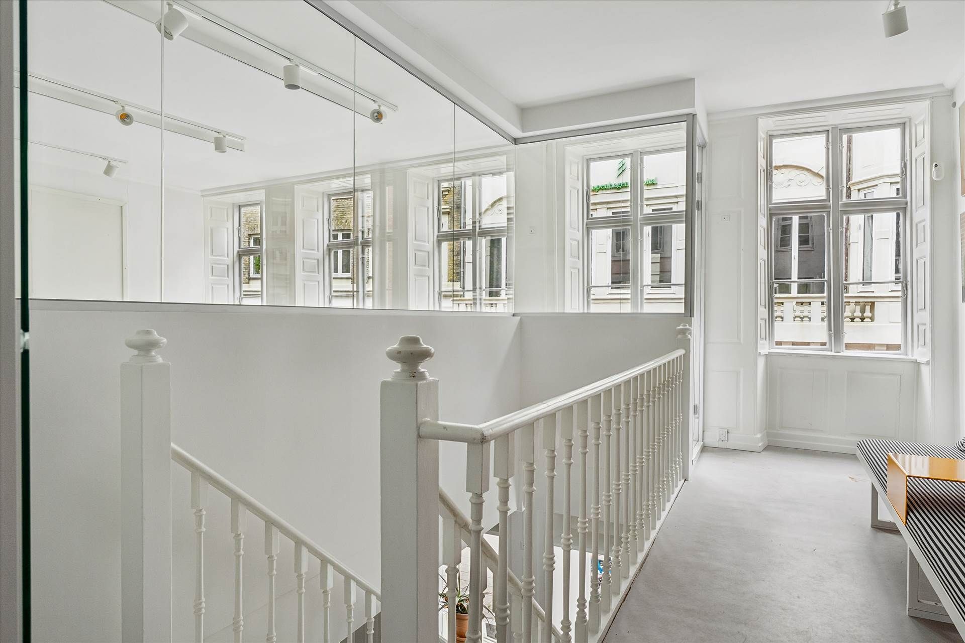 Lys, luftig hall med hvide vægge, gulv og loft, hvide trapper og håndtag, høje vinduer og lysekroner