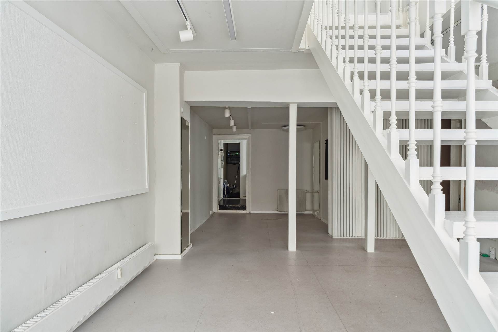 En stor og lys hall med en hvid trappe og lyse loftsbøjler, en hvid væg med et panel og et hvidt radiatorpanel