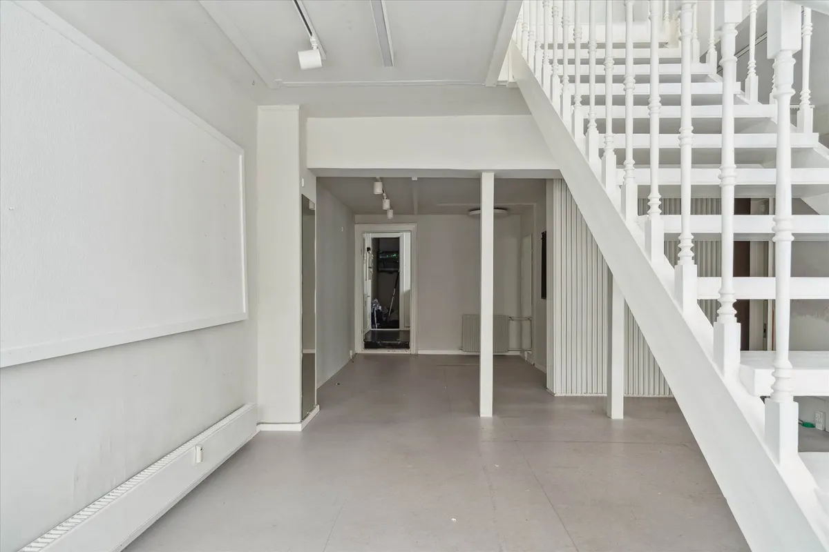 En stor og lys hall med en hvid trappe og lyse loftsbøjler, en hvid væg med et panel og et hvidt radiatorpanel