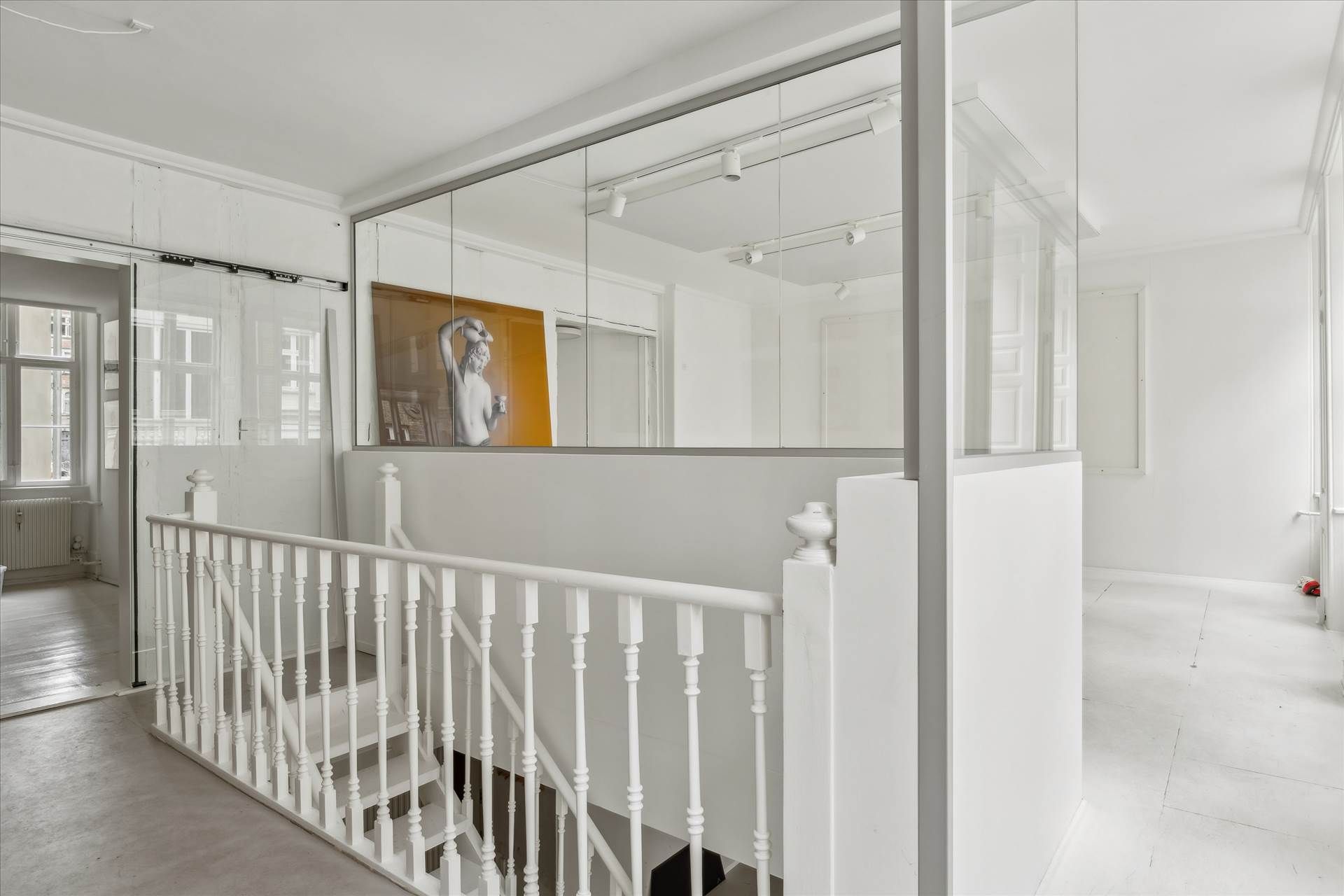 Lyst lejemål med hvide vægge og slanke hvide stige. Der er et stort spejl og en stor maleri i baggrunden