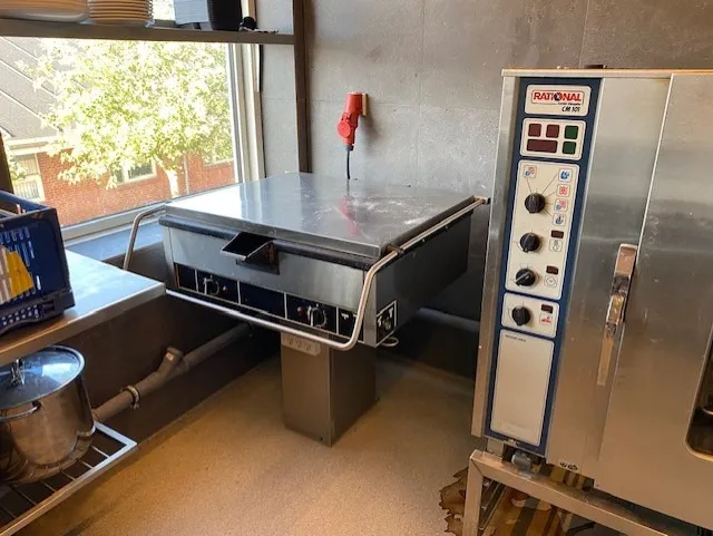 Professionelt køkken med Rational komfur og ovn samt kogegryde og tallerkener på hylden