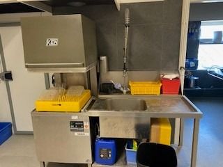 Et stort køleskab med flere sektioner og en maskine til at vaske op. Der er også en stor gryde og andet tøj i farvede kurve