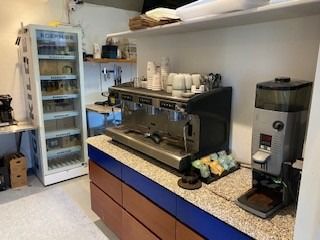 Kaffemaskine, iskøleskab og en række forskelige kopper i et køkken. Der er også en kaffemaskine med en sort top og en hvid