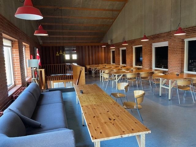 Lyst café med bord og stole samt lysekroner og sofaer i den ene ende