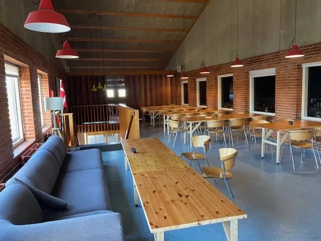 Lyst café med bord og stole samt lysekroner og sofaer i den ene ende