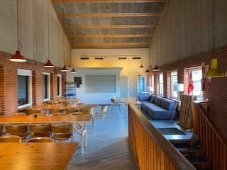 Lyserøde lamper hænger fra loftet, og der er flere borde og stole i rummet. Der er også en sofa og et skrivebord.