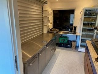 Køkken med flere stålskuffer og en stor køleskab med drikkevarer og et bord med en kaffemaskine.