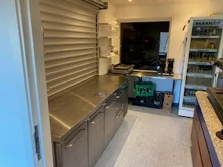 Køkken med flere stålskuffer og en stor køleskab med drikkevarer og et bord med en kaffemaskine.