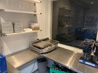 Et moderne køkken med en stålarbejdsplads, kaffemaskine, grill og et vindue med udsigt til et køkken.