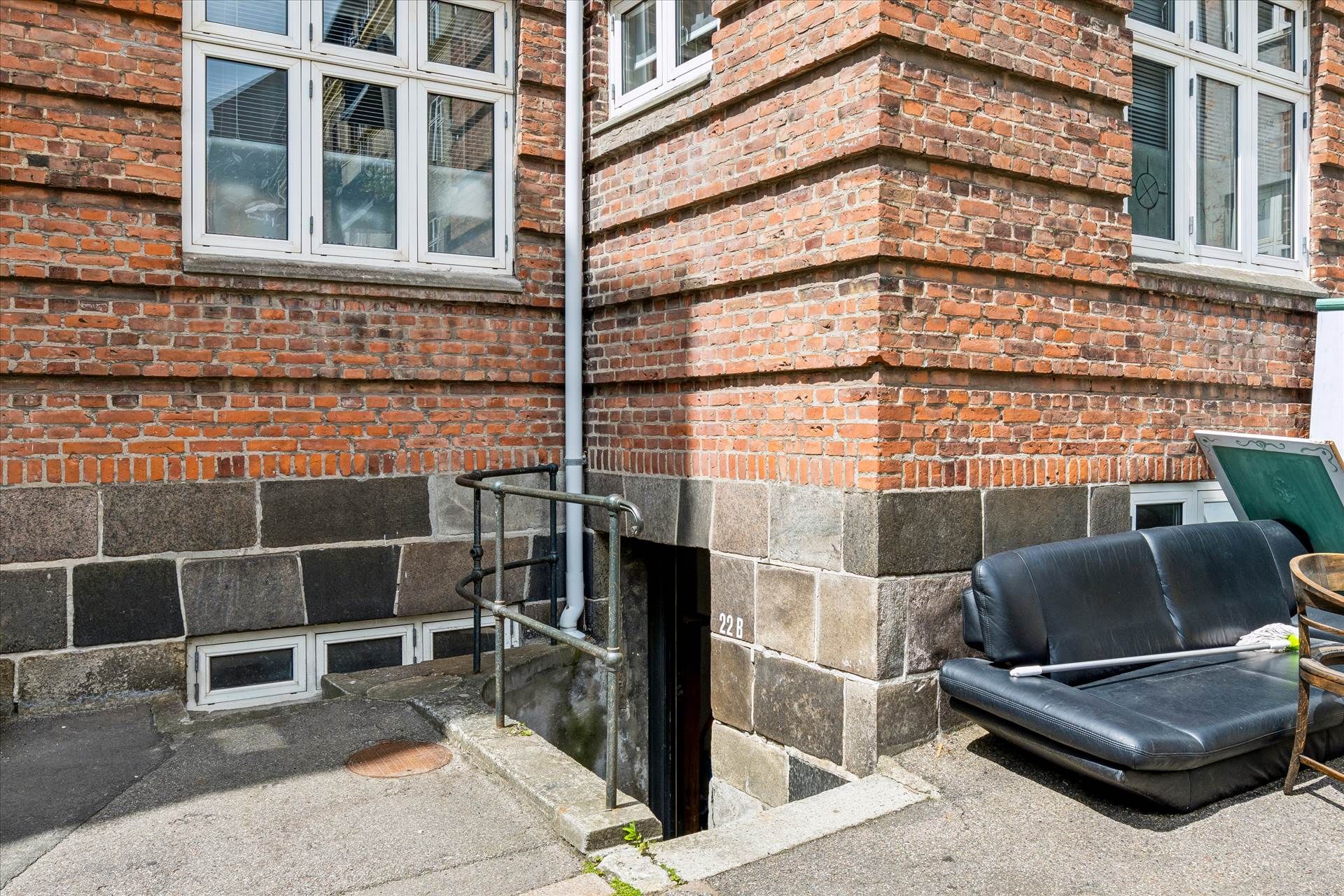 Sort sofa og rengøringsudstyr foran rødmalet hus med vinduer og trin til kælderindgang