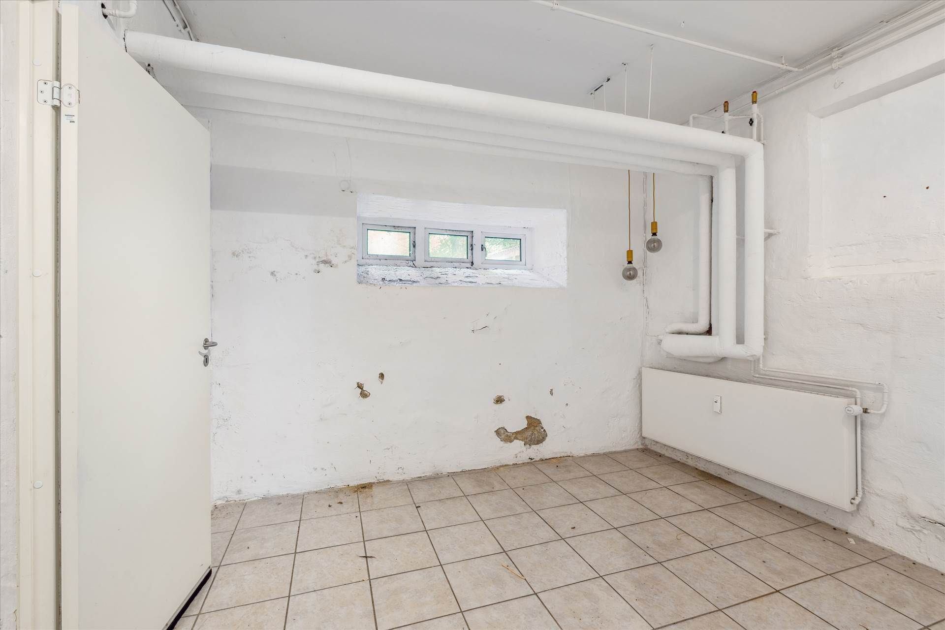 Lagerlejemål med åbne døre og lyse pibesystemer. Tidligere lagerrum med tømrede vægge og lysekroner hængende fra loftet.