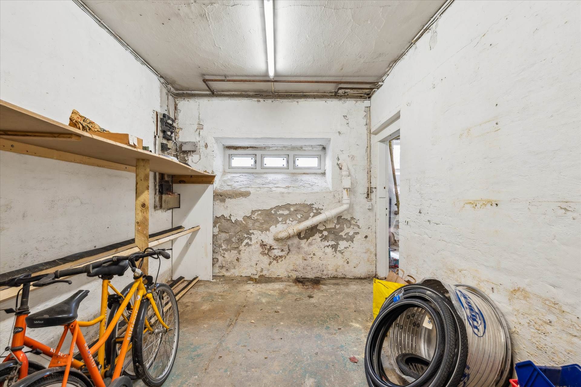 Lagerlejemål med to cykler, gulvmonteret hylde, snavsede vægge og udvendige vinduer