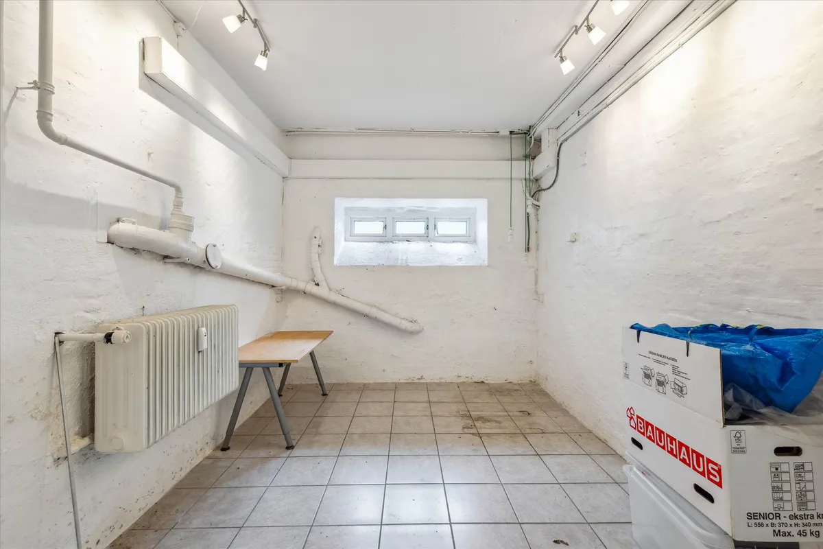 Et lagerrum med en radiator, et bord, et vindue og to bokse med Bauhaus-mærker og en blå pose