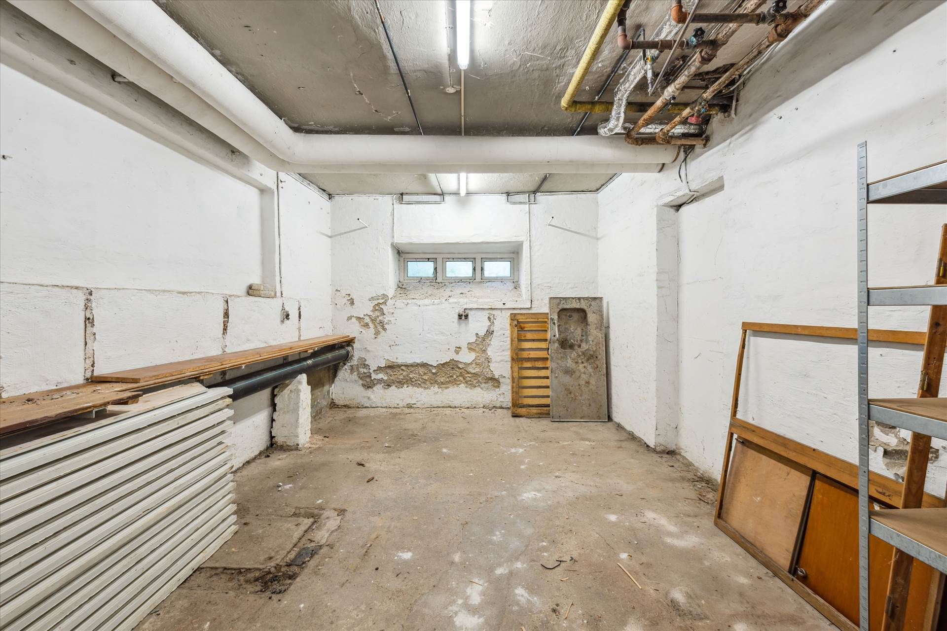 Lagerlejemål med højt loft og store vinduer, indeholder rustne møbler og søjler samt to rækker gulve.