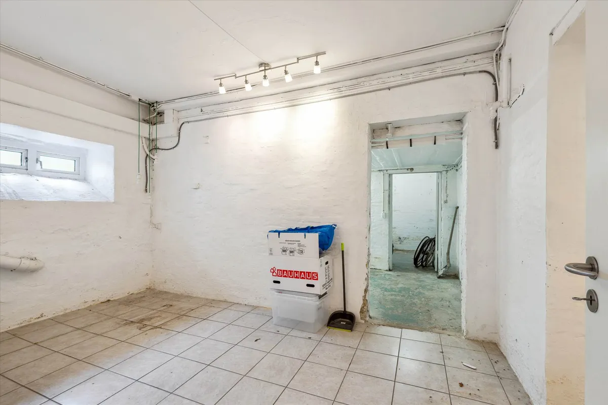 Lagerlejemål med lyse gulve, to Bauhaus-kasser og en støvsugebørste stående ved døren i et lyserum