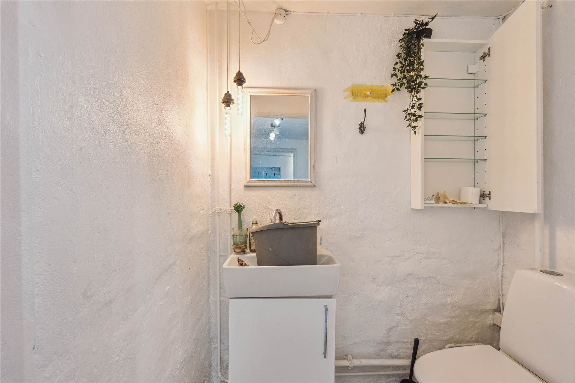 Toiletrum med hvidt badekar, hvidt toilet, hvidt badekar og hvidt badeværelse med spejl og plante samt åbent skab med