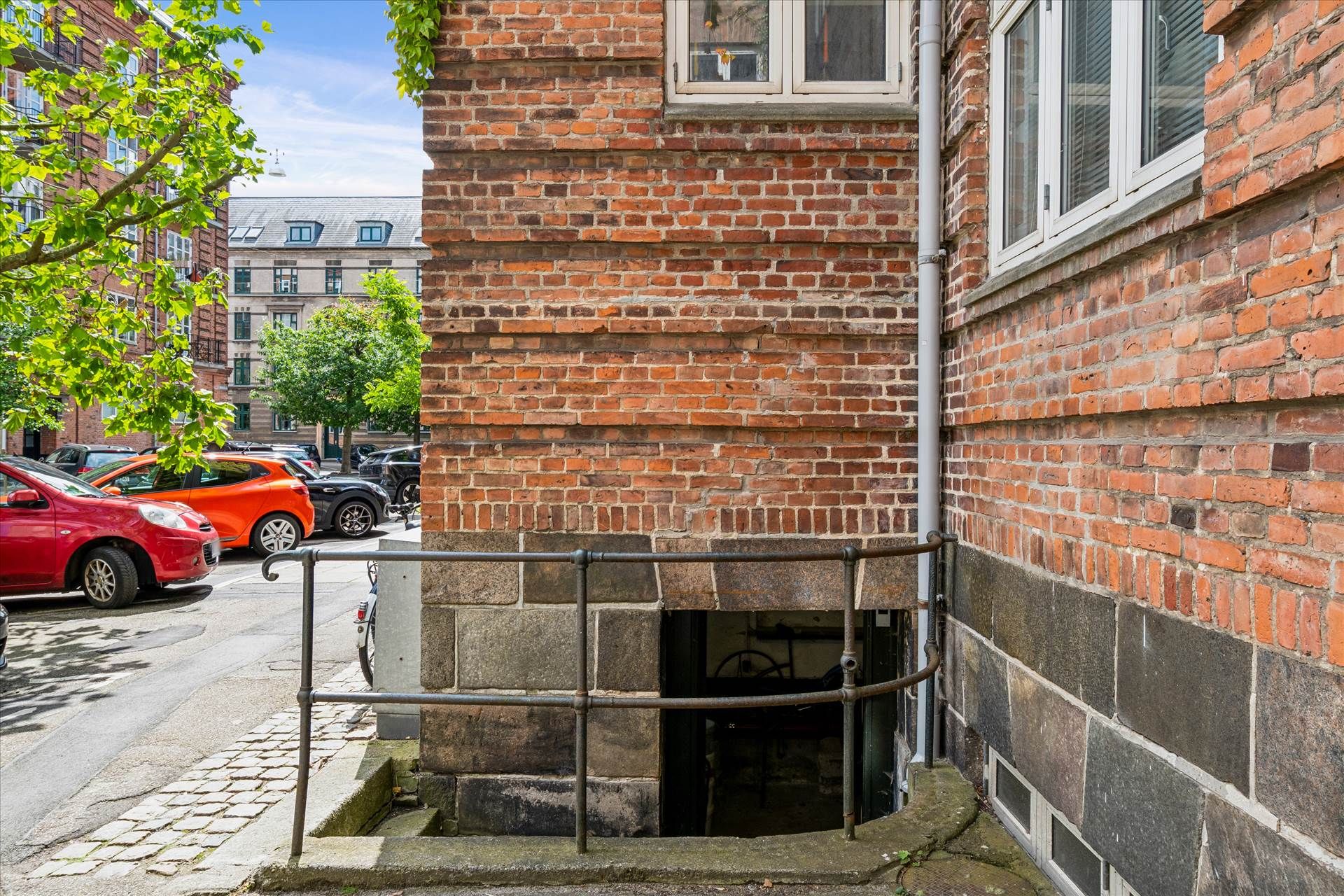 Garageindkørsel til et murstenshus med en trappe og en metalforstærkning foran en garagedør på en smal sidevej