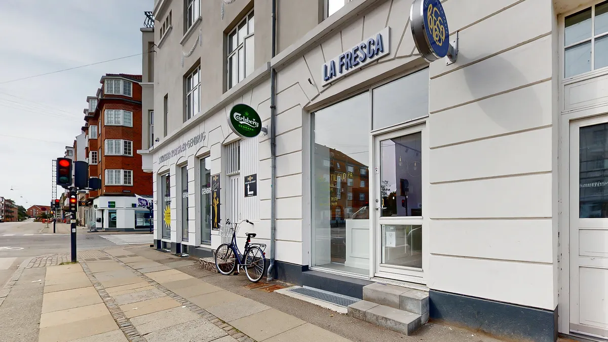 Butik med glasdør og skilt med teksten La Fresca, samt tekst Carlsberg, der står bag ved siden af. En cykel står parkeret på