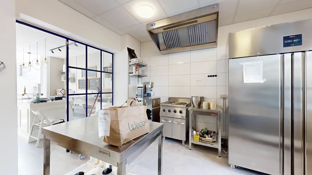 Indkøbsvogn med navnet Wedo på siden står på en metalbord i et moderne køkken med lysegult lys fra loftet og en stor