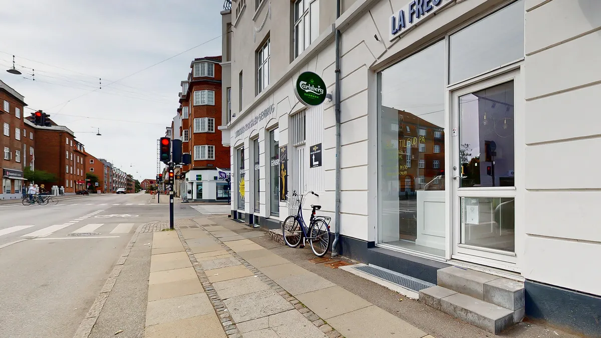 Butik med grøn skilt, der siger Carlsberg, og skrift på døren La Frise på Jernbane Allé, hvor en cykel står parkeret og en