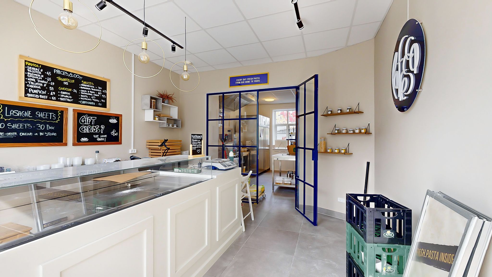 En moderne og hyggelig køkkenudstilling med et køkkenbord, et glaskurv, og tekster på væggen, der fortæller om frisk pasta