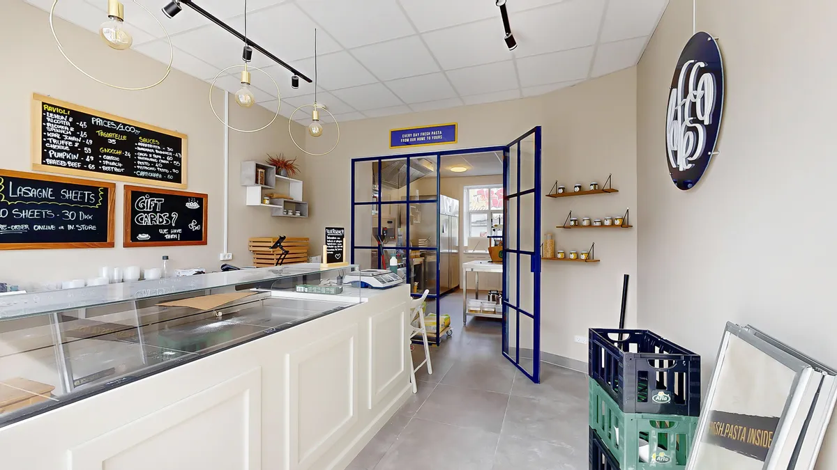 En moderne og hyggelig køkkenudstilling med et køkkenbord, et glaskurv, og tekster på væggen, der fortæller om frisk pasta