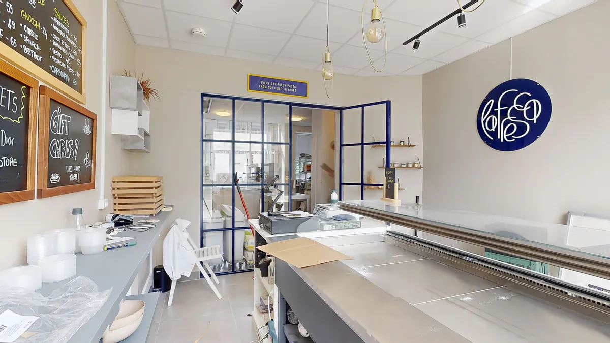 En møbleret og pænt indrettet butik med et bord og en skrivemaskine, samt en papkasse med kop og en stol