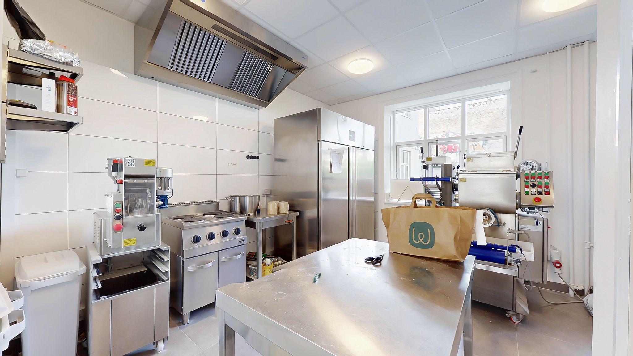 Lejemål med moderne køkken med ovn, køleskab, skabe og stålbord og stålvogne samt papirpose med logo