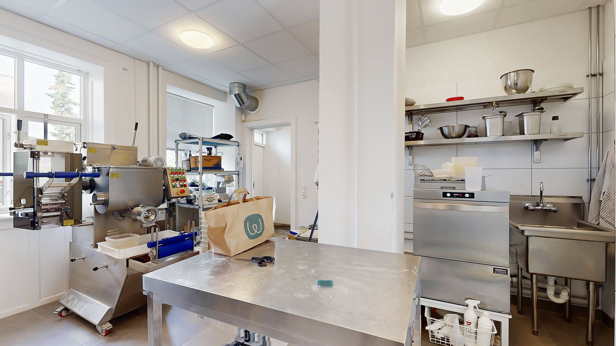Røremaskine og emballagemaskine i en ren og velorganiseret køkkenafdeling med rustfrit stålbord og -skabe