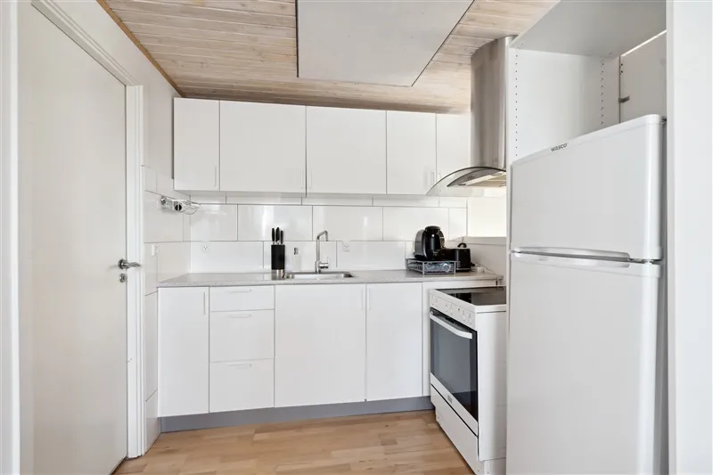 En hvid køkken med moderne møbler, en hvid køleskab, en komfur, et vaskemaskine og et lysekron.