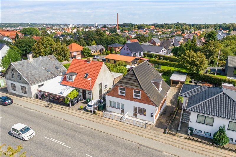Kolding er et smukt område med små huse og mange træer og grønne områder. Vejen er bred med to biler, der kører forbi.
