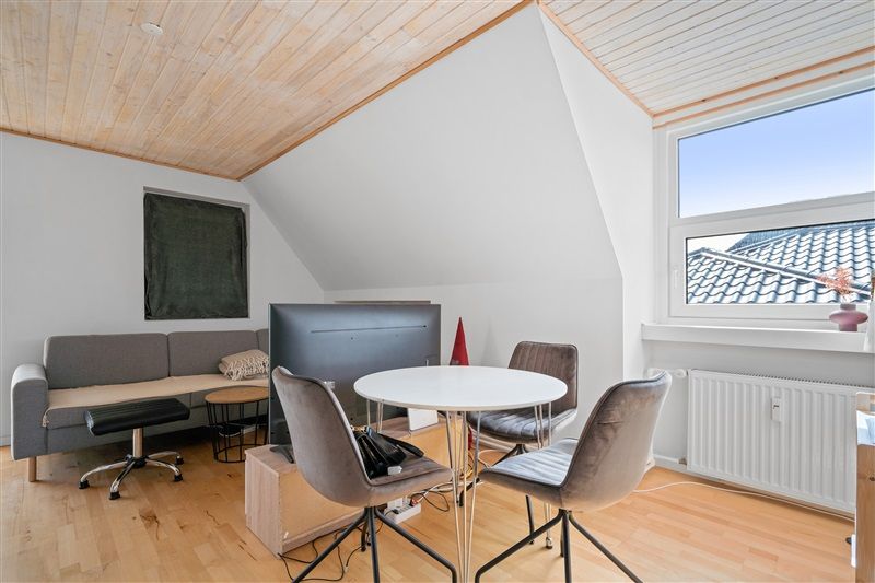 Lille stue med lyse vægge og loft, gulv med møbler og tv, vinduer og radiatorer