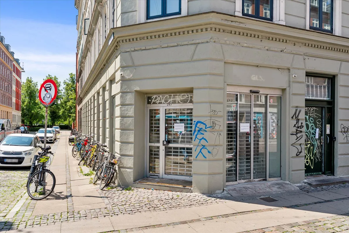 Bygning med flere cykler og graffiti i en gade med biler og en grøn plante i baggrunden