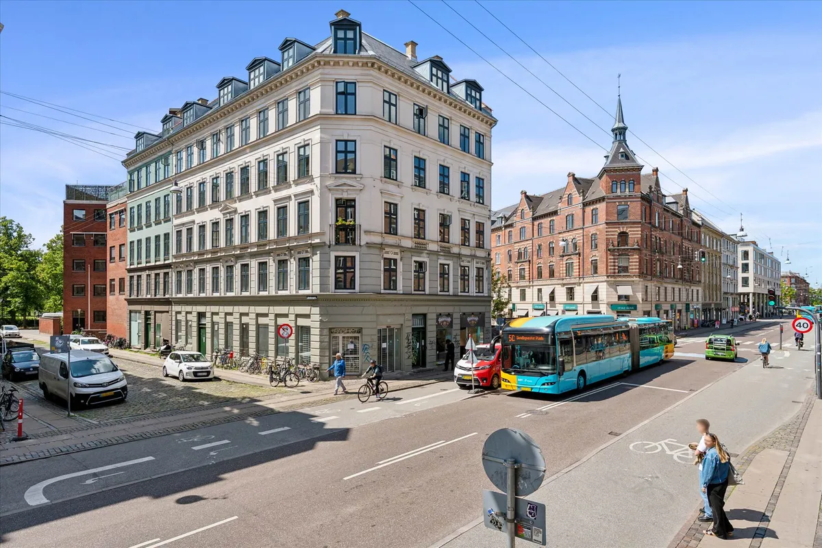 Biler og busser kører på en bred gade med adgangsforbudsskilte og folk krydser en gågade.