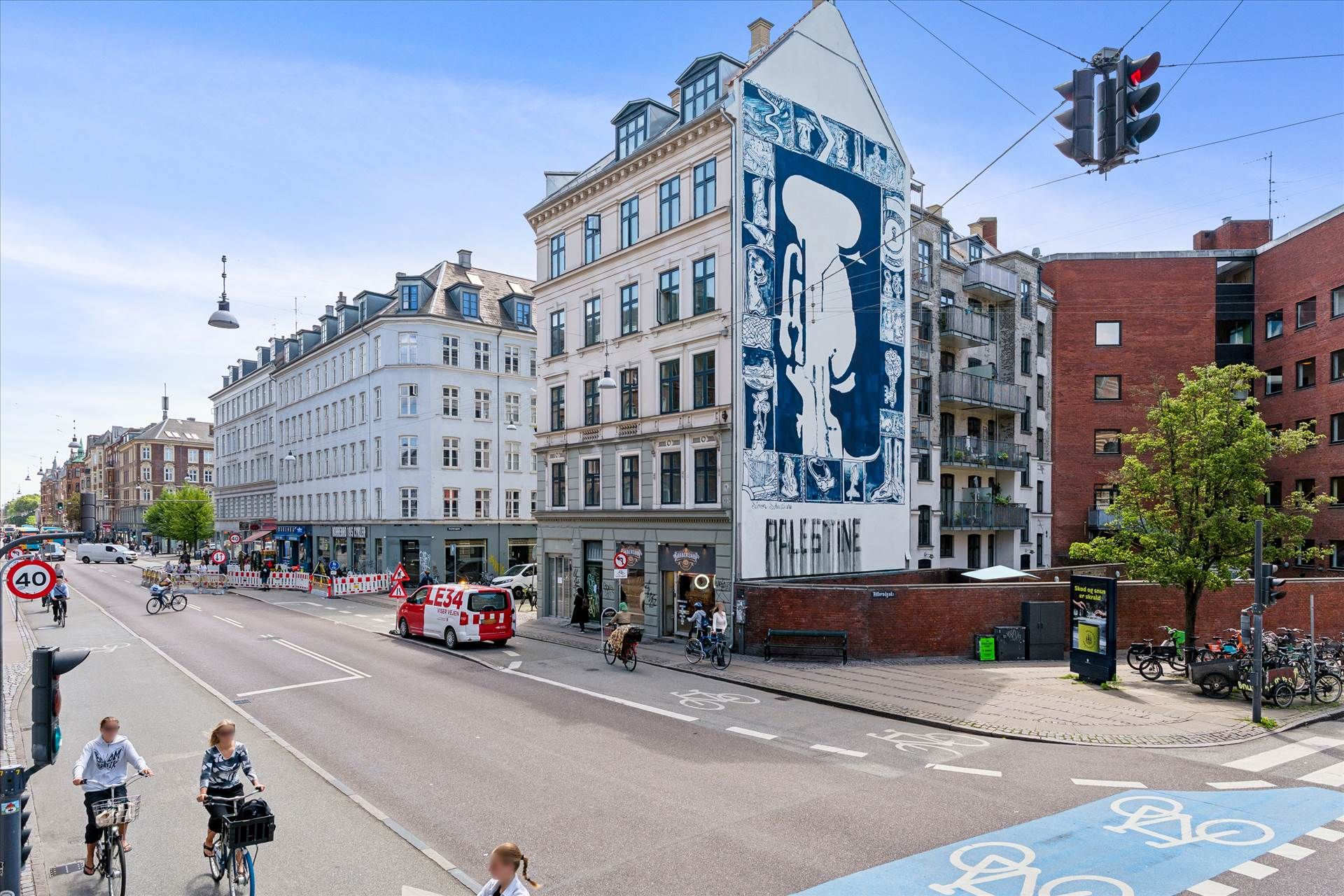 To cyklister kører på gaden med 40 km/t-skilt og trafiklys og et mural med ordet Palæstina