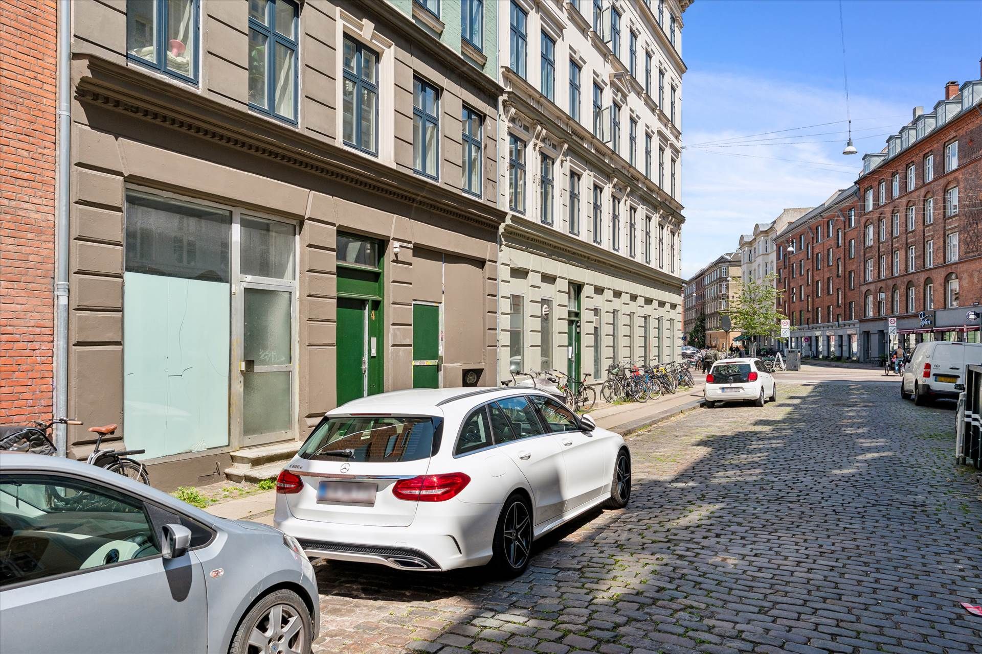 Forskellige biler parkeret på en gammel stenbro og en hjørnebygning med flere vinduer og grønne døre