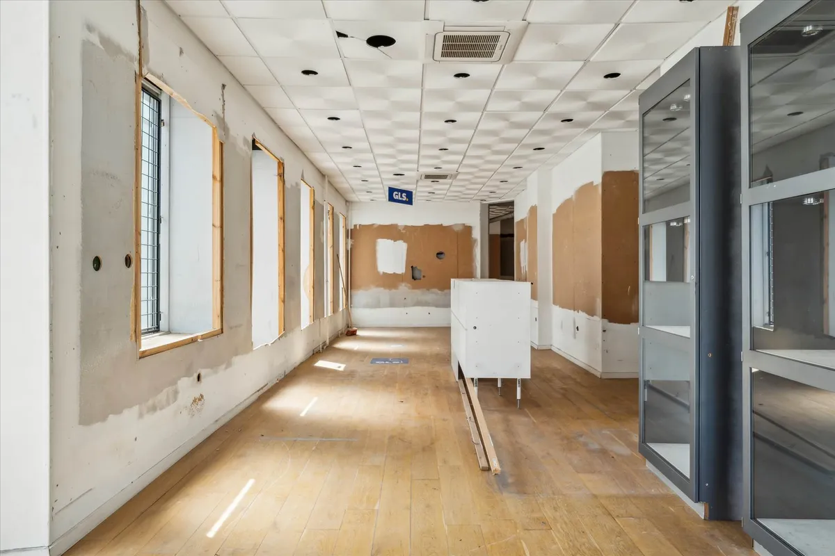 En tom og renoveret erhvervslokal med højt loft og vinduer, hvor væggene og gulvet er i reparation