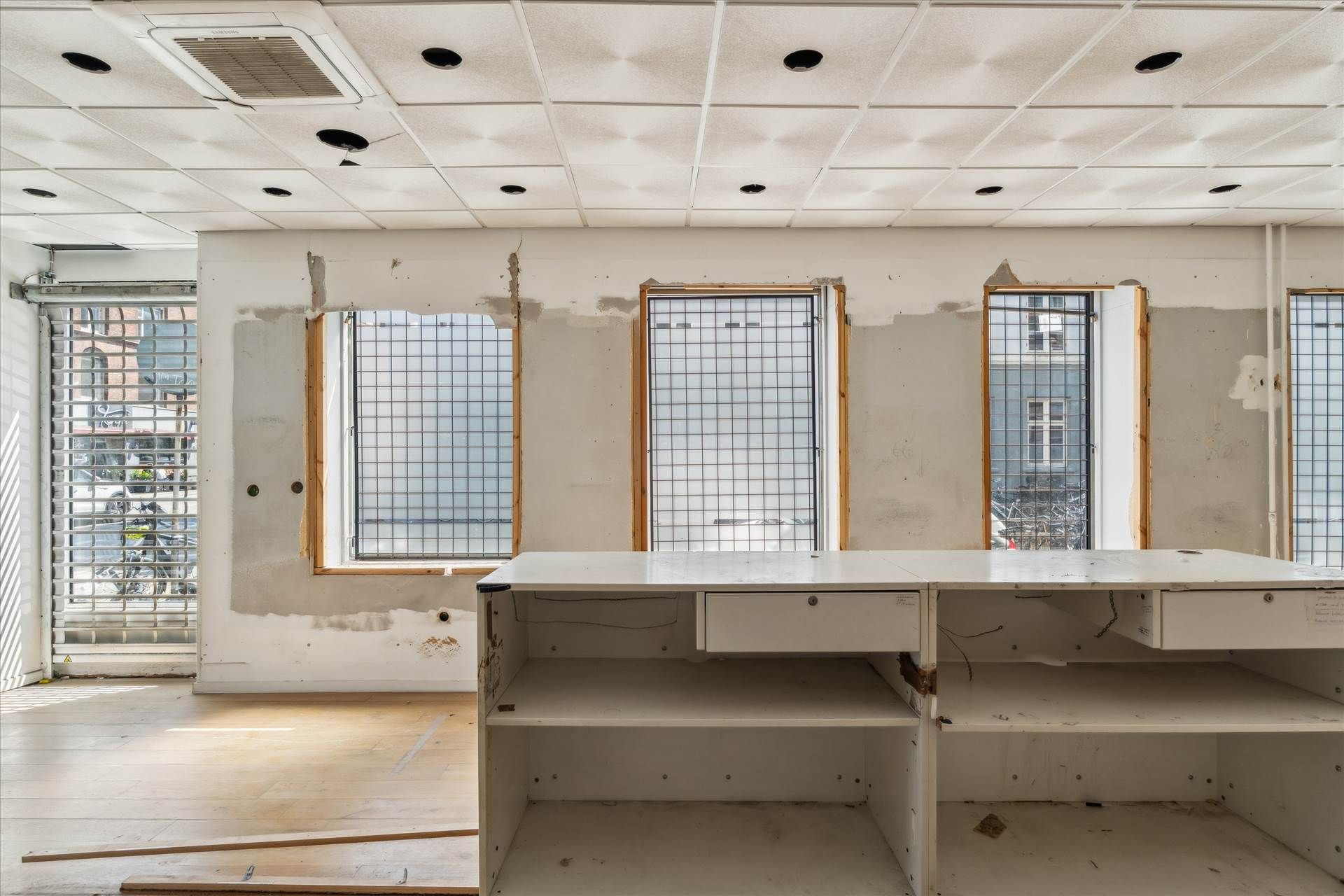 En tom erhvervslokal med fire vinduer og hvide vægge samt en lyseblå loftsventilator