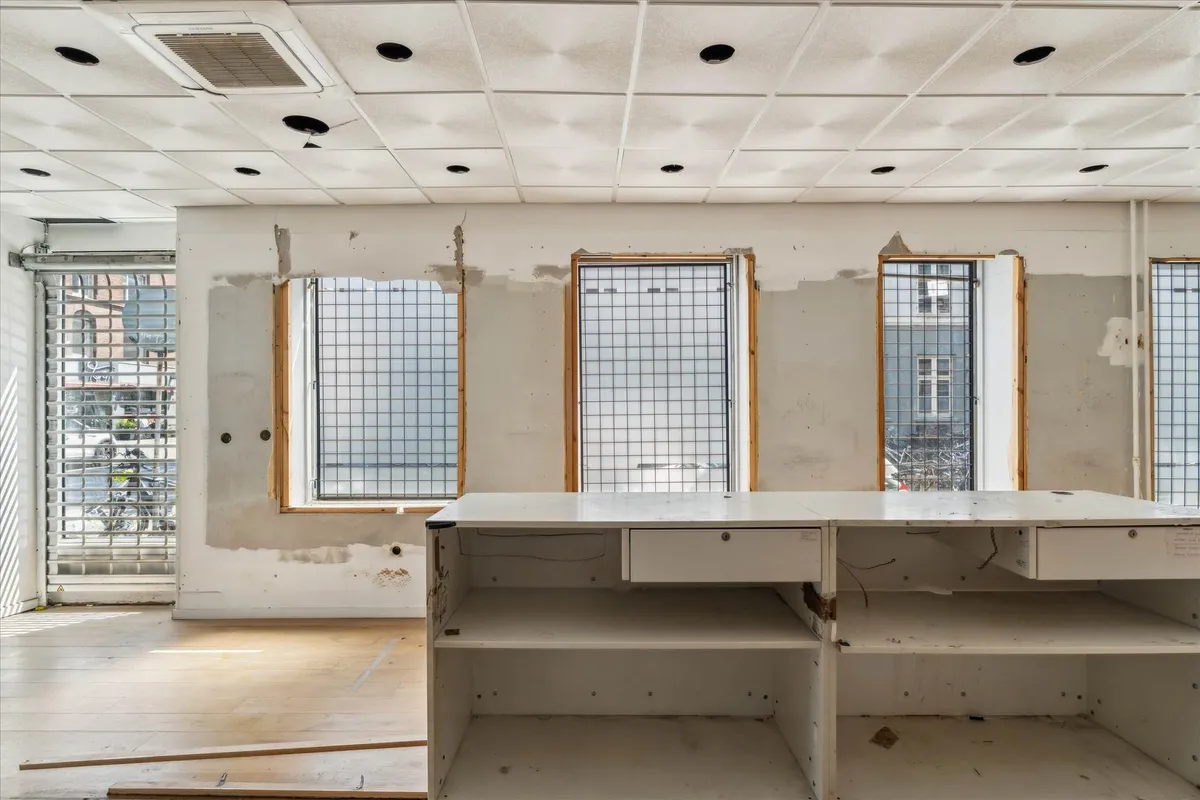 En tom erhvervslokal med fire vinduer og hvide vægge samt en lyseblå loftsventilator