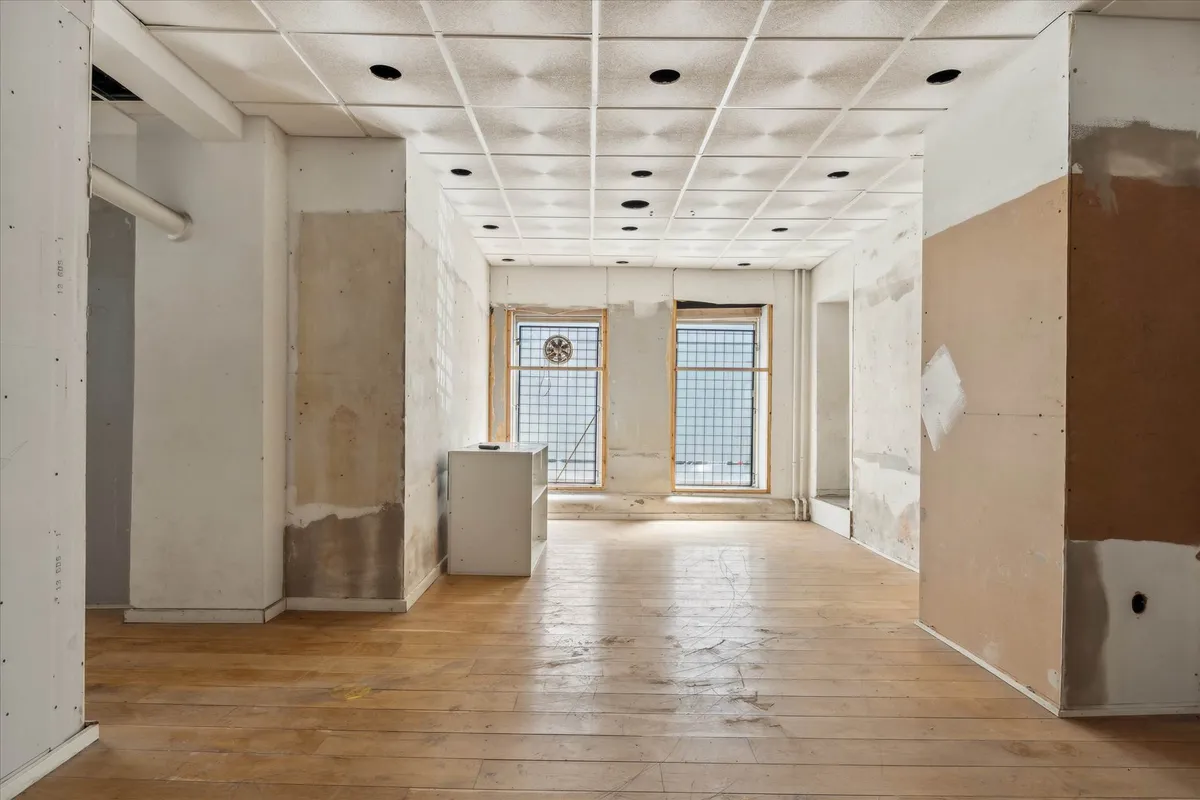 Et stort, tomt erhvervslokale med lysegul gulvbelægning og hvide vægge i renoveringsfasen