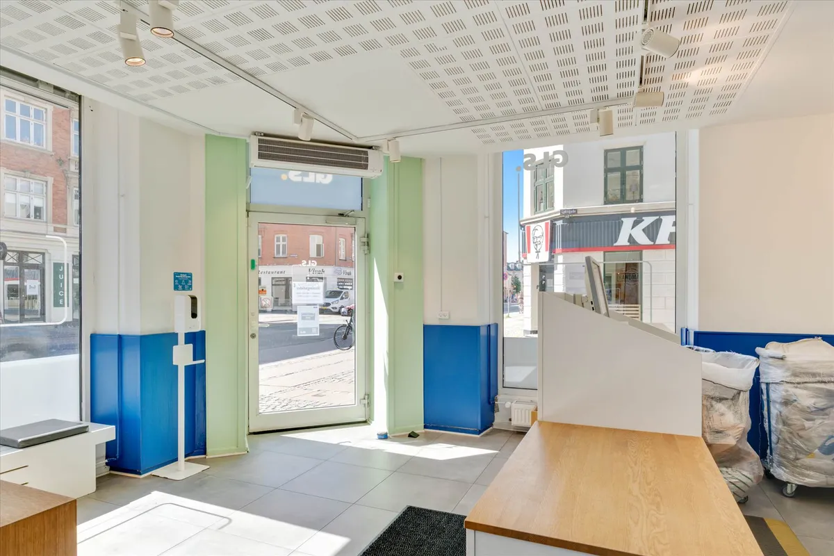 Indgang til et forretningslokale med glasdøre og gulvbelægning af marmor og en træbar i forgrunden. En