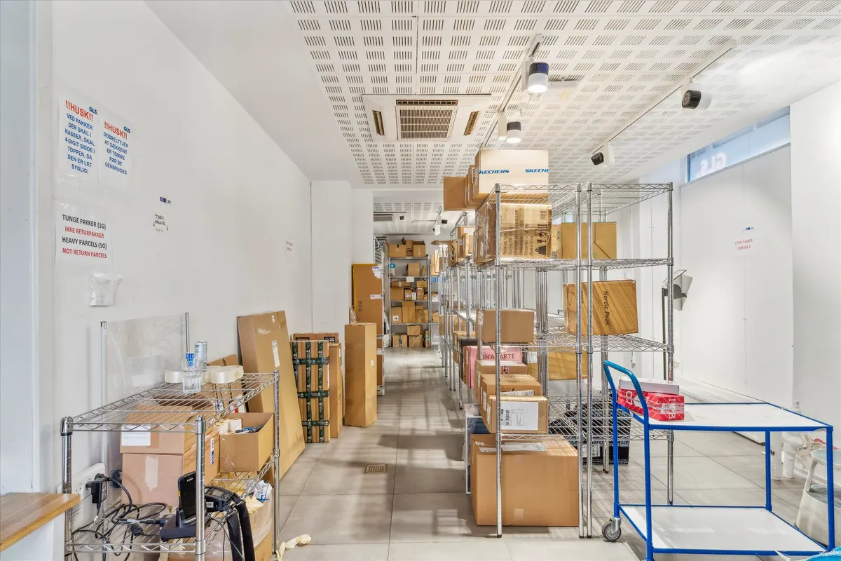Lager med kartoner og emballagematerialer, og en rullebrod, stående i et stort rum med højt gulv og hvide vægge